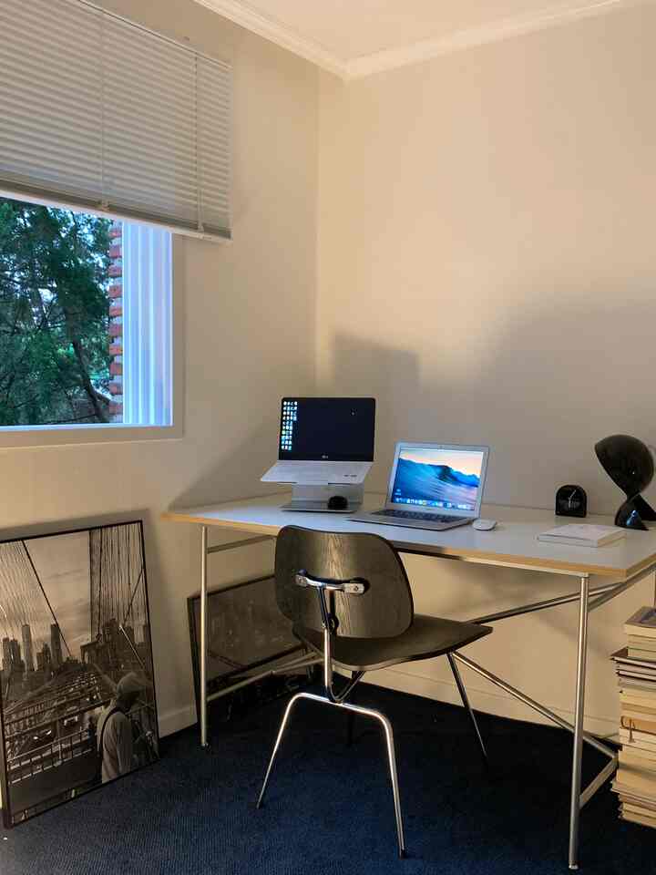 白とダークブルーの色調のモダンなホームオフィス、シンプルなデスクと椅子、アルミブラインド、ポスターが配置された落ち着いた作業空間