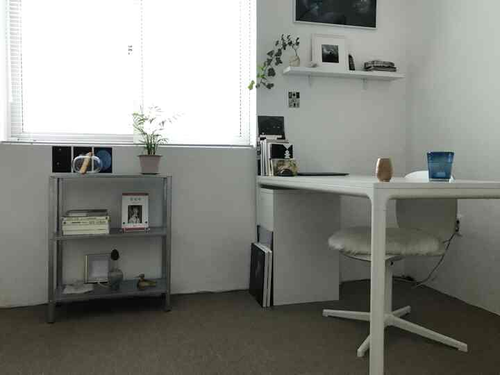 White and gray toned small home office space featuring a simple desk, shelf, and potted plant with a clean minimalist atmosphere