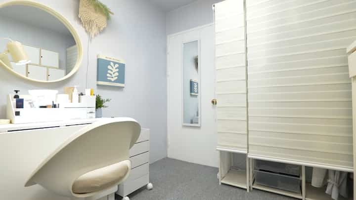 白とナチュラルモダンのトーンのウォークインクローゼット、化粧台と丸い鏡、快適な椅子が配置された清潔感のある空間