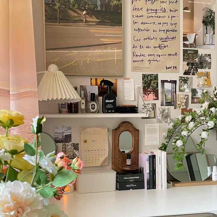 ナチュラルトーンのワンルーム、白いデスクにポスター、造花、本、鏡が配置された雰囲気のある作業空間