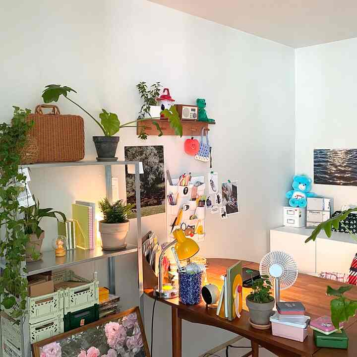 White-walled natural wood home office space featuring multiple plants and wall art creating a cozy workspace