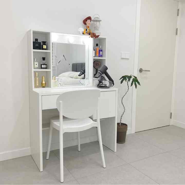 白いトーンの寝室、LED照明付きの化粧台と椅子、観葉植物が配置されたシンプルなインテリア