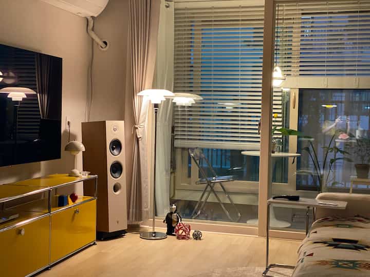 A modern natural living room featuring a yellow TV stand and wood tone flooring, complemented by a transparent chair and floor lamp creating a cozy atmosphere