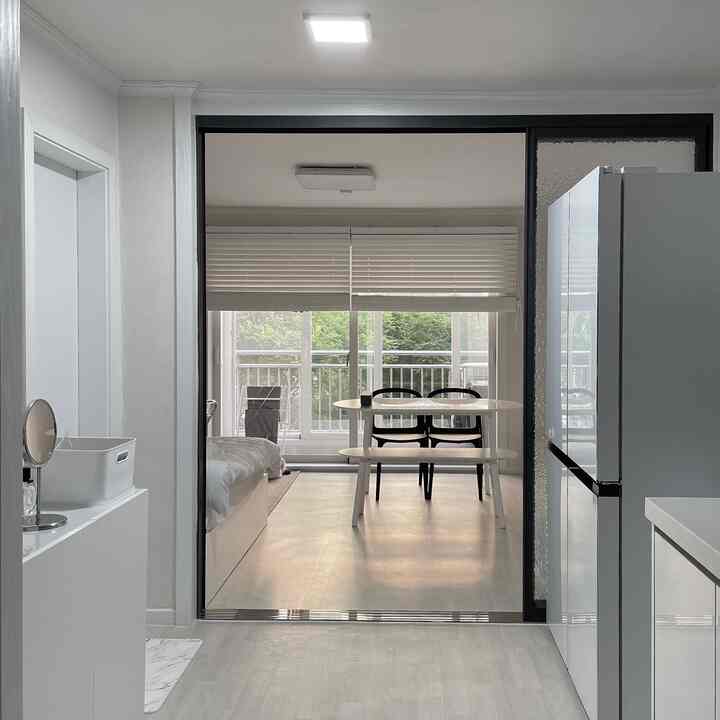 White-toned entrance and kitchen space featuring a simple dining table and cabinetry with a minimalistic interior