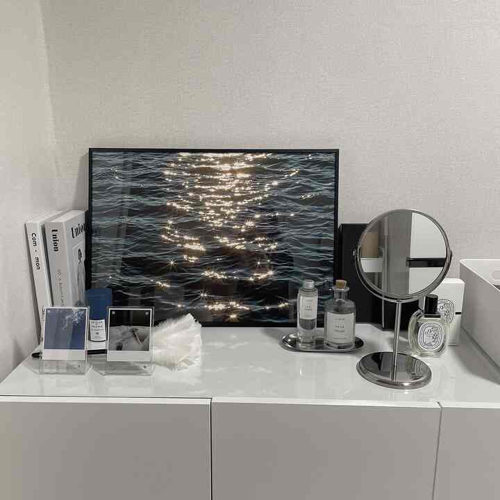 明るいホワイトトーンのトイレ横の空間にチェスト、額縁、丸い鏡、ディフューザーが整えられたシンプルで清潔感のあるインテリア