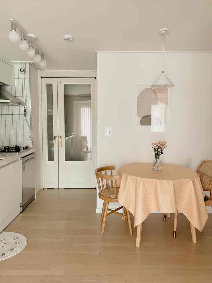 明るいアイボリーと木目調の温かみのあるキッチン、丸いダイニングテーブルと木製の椅子が配置された自然な雰囲気の空間