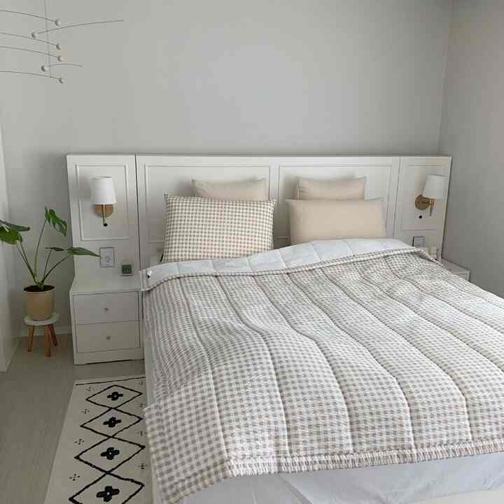 ベージュトーンの寝室、中央にベッドとチェック模様の寝具が配置され、両側にナイトスタンドと壁灯があるホテルライクな空間