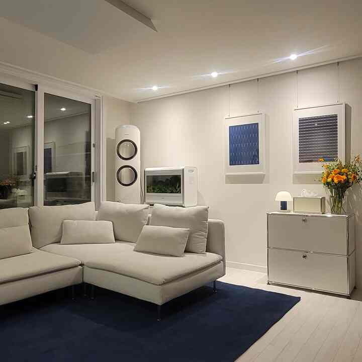 ホワイトトーンのリビング、ネイビーのラグとベージュのコーナーソファが配置されたミニマルでモダンなインテリア