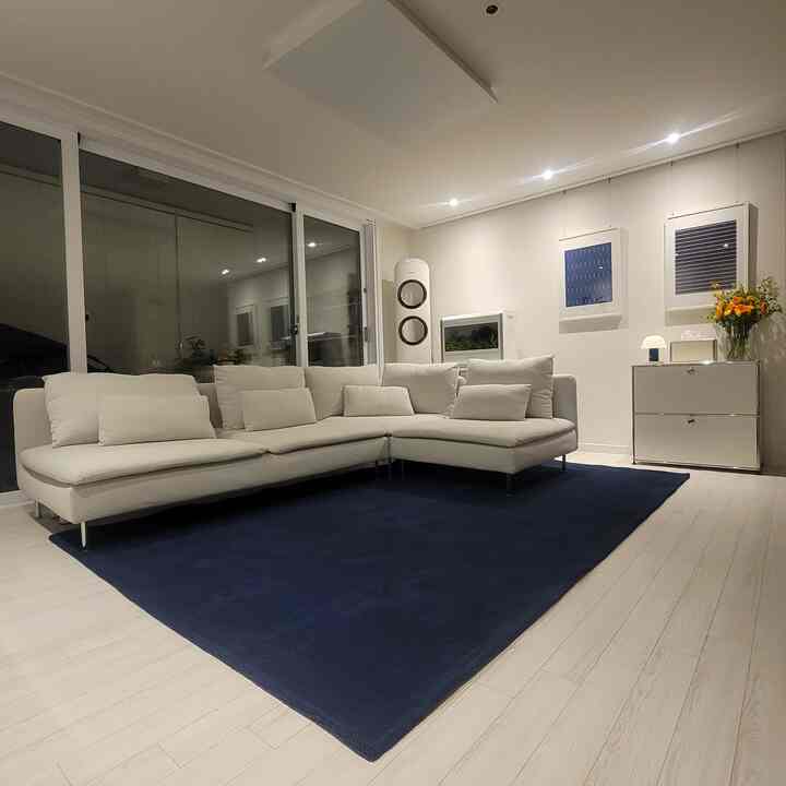 白とネイビーの色調のリビング、大きなコーナーソファとネイビーのラグが配置された、清潔で温かみのあるナチュラルモダンなインテリア