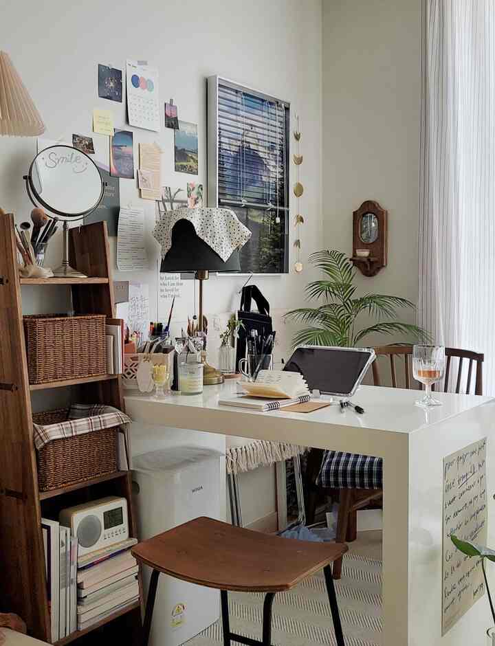A cozy studio apartment home office space featuring white and wood tones, decorated with plants and personal accessories