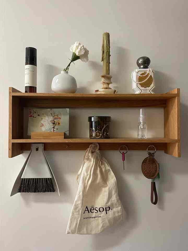 Natural-toned entrance wall shelf with organized cleaning broom, picture frame, and perfume bottle, creating a neat space