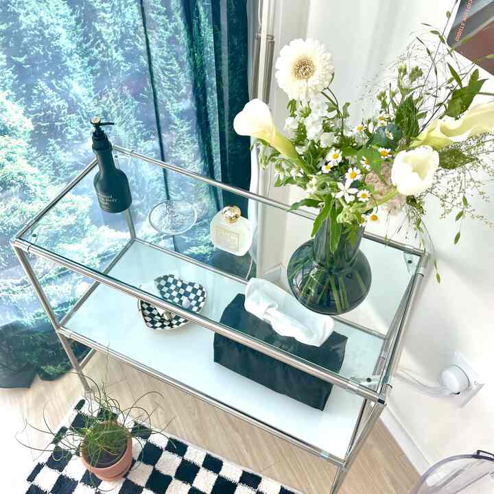 Sky blue-toned space featuring transparent glass shelves, metal frame, and decorative plants with a clean interior vibe