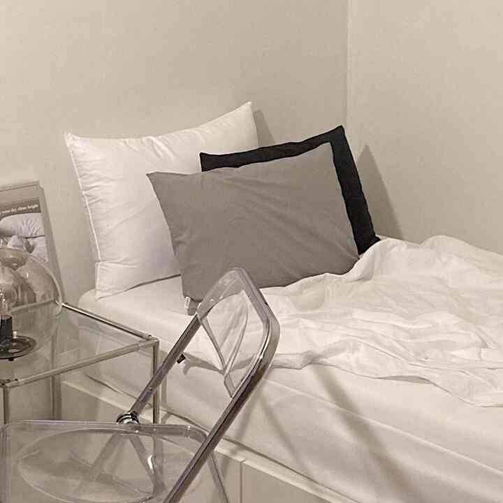 モノトーンの寝室、白いベッドとグレー・黒の枕、透明の椅子が配置されたシンプルなインテリア