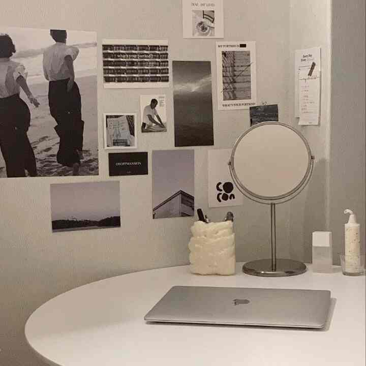 ホワイトの円形テーブルとポスターがあるシンプルなホームオフィス空間、壁には鏡と絵葉書が配置されている