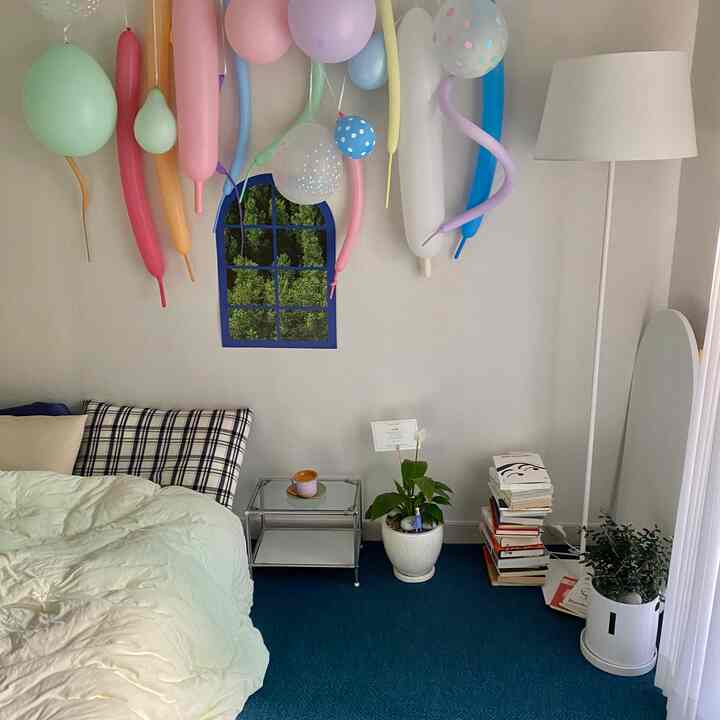 ネイビーのカーペットとアーチ型のポスターが配置されたワンルーム寝室、本の山と植物がアクセントの雰囲気あるインテリア