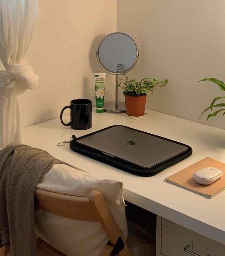 白とベージュのトーンが印象的な寝室のシンプルなデスク、ノートパソコンと植物が配置された落ち着いたホームオフィス空間