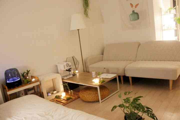 ナチュラルな色調のリビングルーム、2人掛けソファと木製テーブル、フロアランプと植物が配置された落ち着いた空間