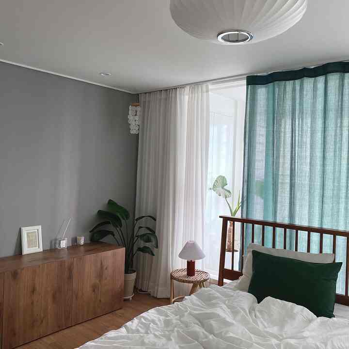 A white and green toned bedroom featuring wood-toned furniture and plants, creating a natural and serene atmosphere