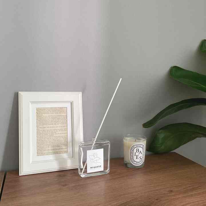 グレーの壁とブラウンの木製テーブルに、白い額縁、透明なディフューザー、キャンドルが配されたシンプルで落ち着いたホームギャラリー空間