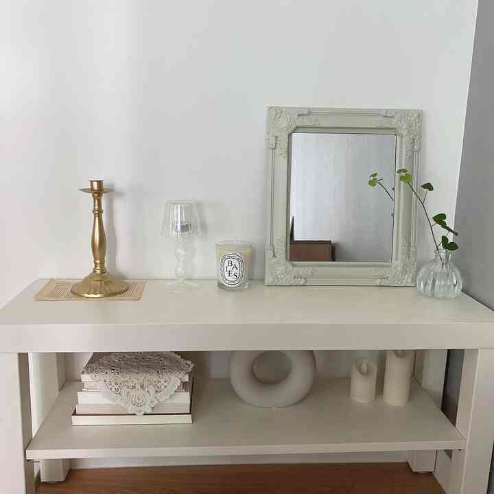 ホワイトトーンの棚にゴールドのキャンドルホルダー、キャンドル、鏡、花瓶が置かれたシンプルでナチュラルな雰囲気のインテリア
