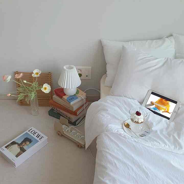 A white and natural tone bedroom featuring a bed with white bedding, an iPad, and dessert creating a cozy, minimal atmosphere
