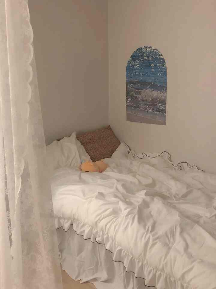 白を基調とした落ち着いた寝室、アーチ型のポスターとレースカーテン、フリルの寝具が配置された雰囲気のあるインテリア