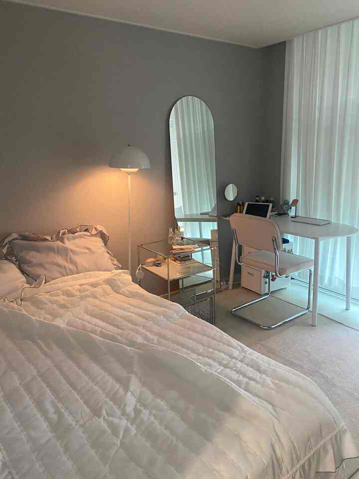 Calm gray-walled bedroom featuring white furniture including plush bed, desk, nightstand, and long sheer curtains