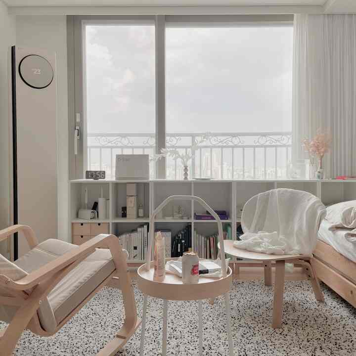 Bright and serene living room in white and wood tones featuring minimalist furniture and bookshelf under large windows