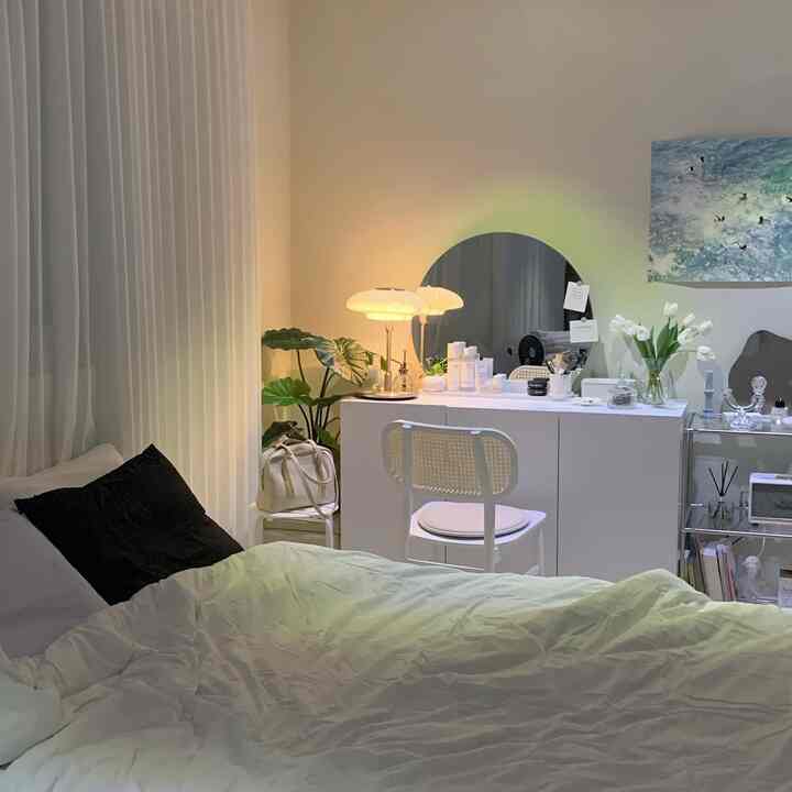 白を基調とした寝室、丸い鏡のある化粧台と柔らかな照明が配置され、落ち着いたシンプルな印象の空間