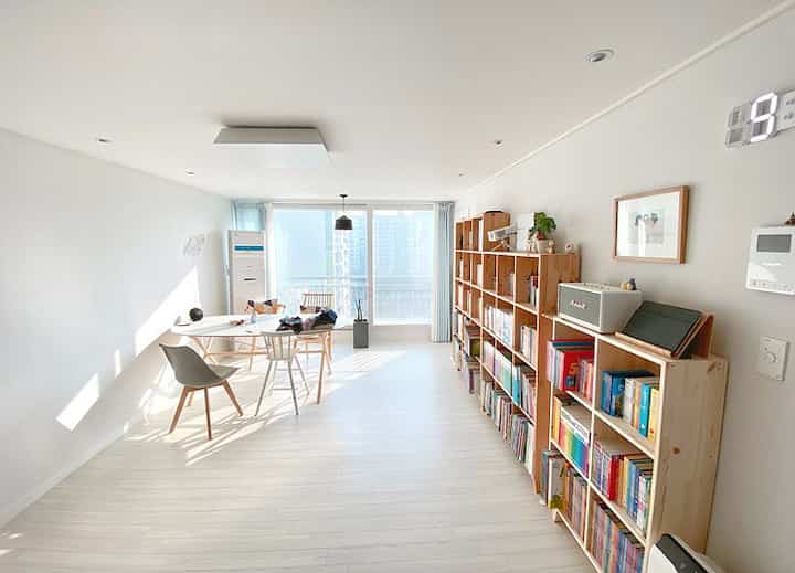 Bright and spacious Nordic-style living room in white and wood tones, featuring a large bookshelf and dining set