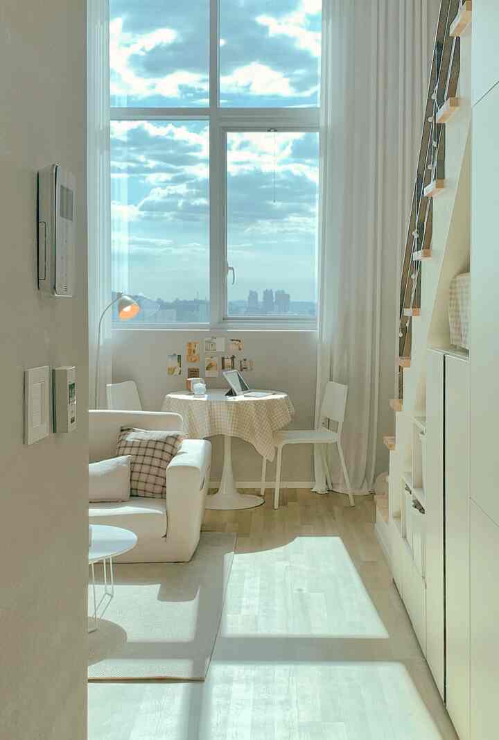 Bright white and natural toned small studio apartment featuring a sofa and round table, creating a cozy home cafe atmosphere