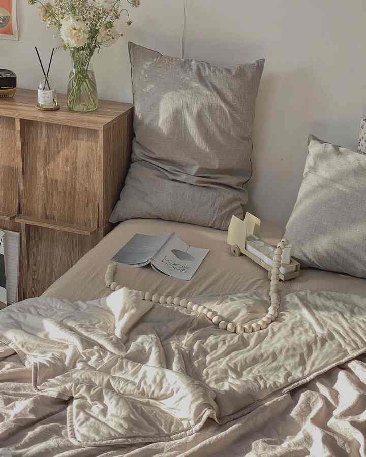 ナチュラルカラーの寝室、枕と寝具が置かれたベッドと木製収納キャビネットが配されたシンプルなインテリア