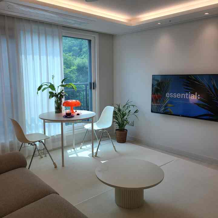 白を基調としたリビング、丸いダイニングテーブルと白い椅子2脚、コーヒーテーブル、グリーンの植物が配置された明るく清潔感のあるインテリア