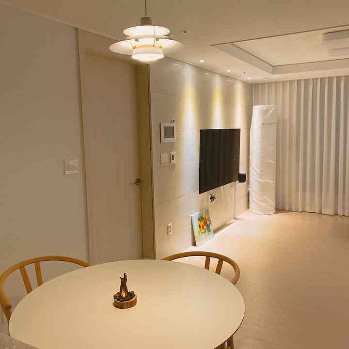 ホワイトと木目調のリビング兼キッチン、丸いダイニングテーブルとラタンチェアが配置された、居心地よくシンプルな新婚の家のインテリア