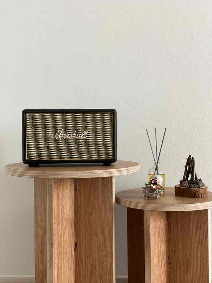 白い壁と木目調のリビングルーム、丸テーブル上にBluetoothスピーカーとディフューザーが配置された雰囲気のあるインテリア