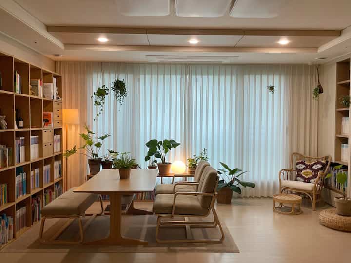 Natural wood tones and beige curtains in a living room featuring large bookshelves and sofa table with a warm relaxing atmosphere