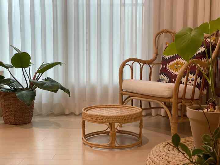 Natural tone study space with white curtains background, rattan armchair and round floor tea table, plants creating a cozy atmosphere