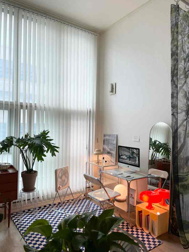 白と透明感のあるモダンなワンルームのホームオフィス、チェッカーボードのラグと植物が配置されたシンプルな空間