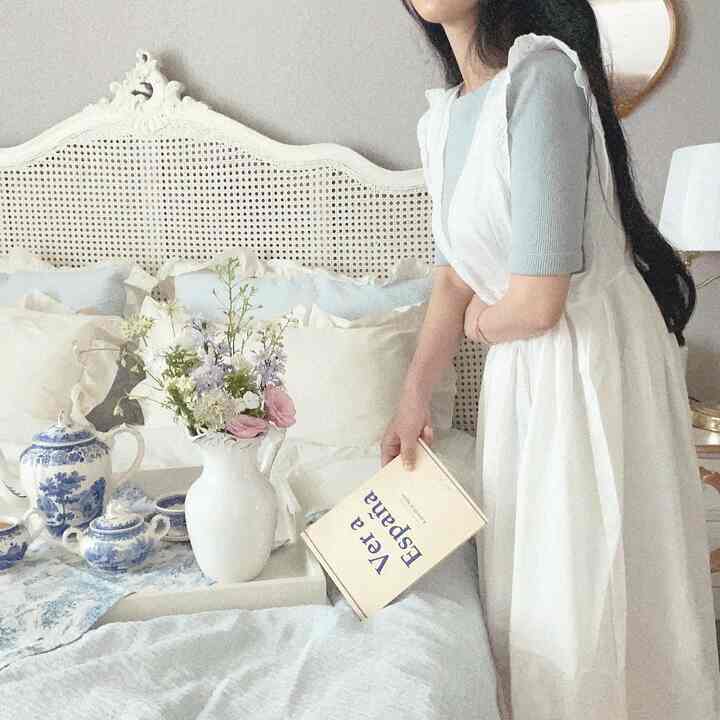 A white and blue toned bedroom featuring French Country style vintage decor, soft pillows, and elegant bedding with a cozy atmosphere