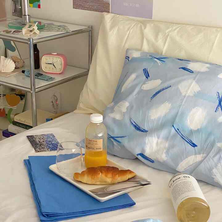 White and blue toned bedroom with a cozy tray featuring orange juice and croissant, creating a warm atmosphere