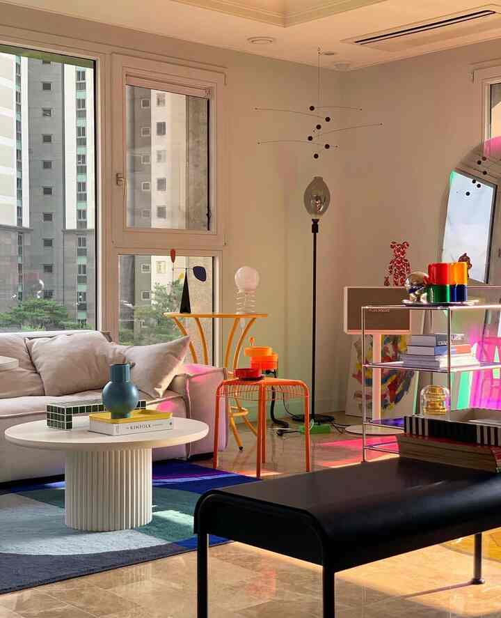 白い壁と茶色の大理石フロアが調和したモダンなリビング、円形のコーヒーテーブルとカラフルな小物が配置された活気ある空間