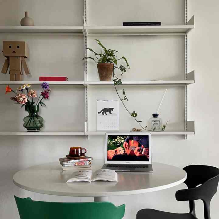 White-toned kitchen space featuring a round table, chairs, and shelves with plants and objects in a minimal atmosphere