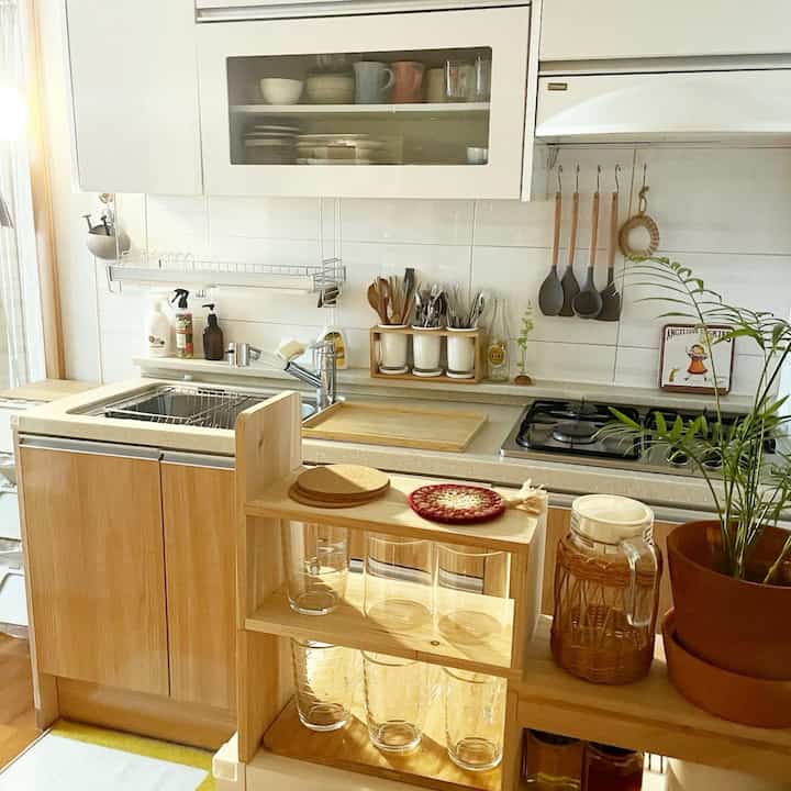 Natural wood tone and white tiled kitchen featuring compact storage and cooking utensils arranged in a warm atmosphere