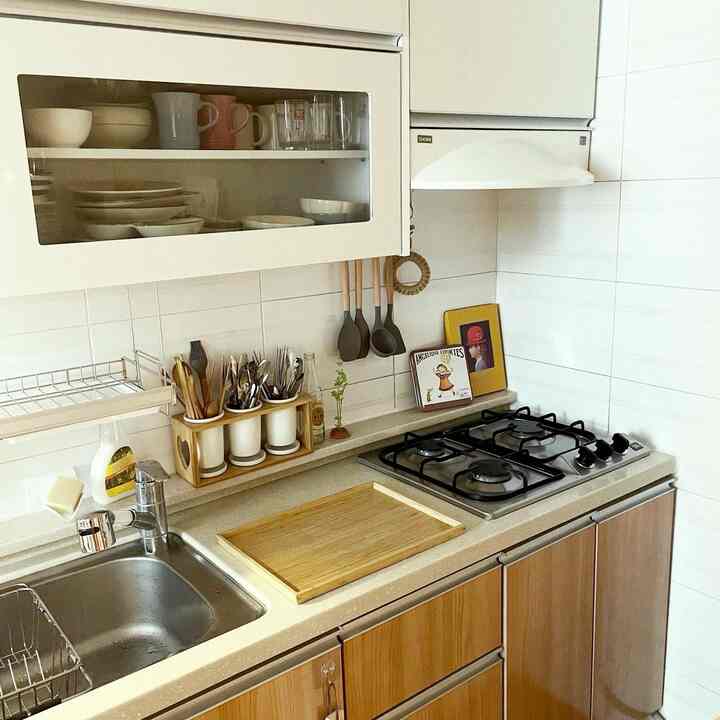 Natural wood tones and white tiled kitchen featuring organized kitchen utensils and bamboo tray with a clean practical atmosphere