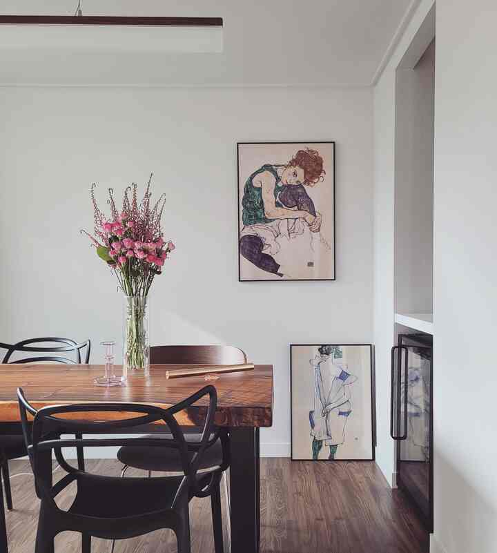 Wood tone dining room featuring a wooden dining table, black chairs, vase with flowers, and framed artwork, creating a clean natural atmosphere