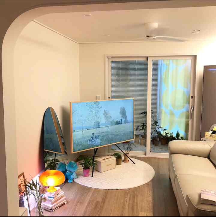 Warm white-toned living room featuring a beige sofa, round rug, full-length mirror, and plants creating a bright and tidy space