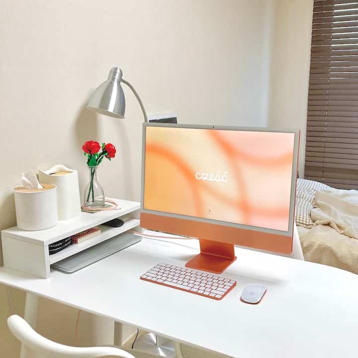 Bright orange iMac on a white desk in a compact bedroom-style home office space