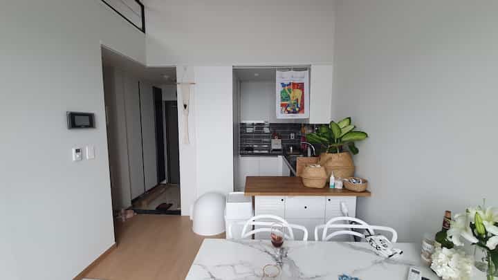 明るいホワイトとナチュラルウッドトーンが調和した小さな二人暮らし向けのキッチンとダイニングスペース、ペット用品が配置された雰囲気のあるインテリア