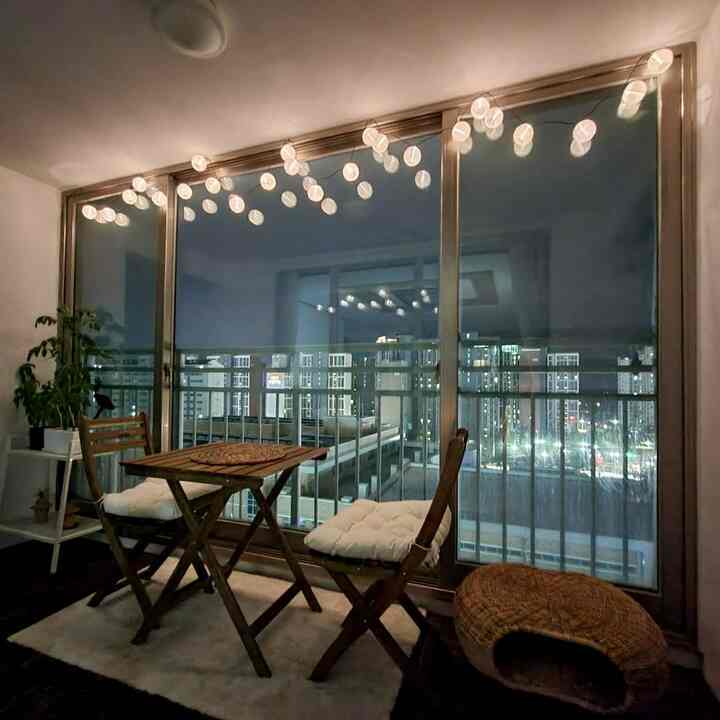 Natural wood tones and beige rug define a cozy veranda home cafe space with string lights and outdoor table set.