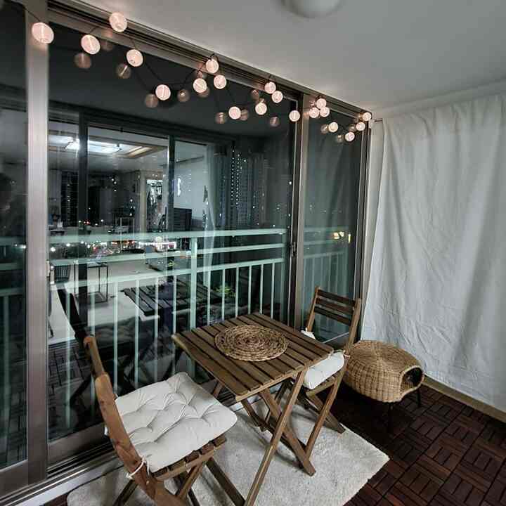 ナチュラルな木目調のバルコニー、アウトドアテーブルとチェア、ペットハウス、ストリングライトが配置された雰囲気のある空間